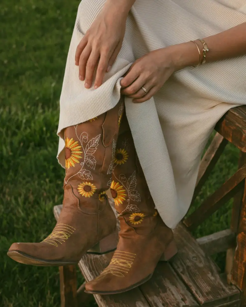 Close-up of brown cowboy boots with embroidered sunflowers under a cream knit dress