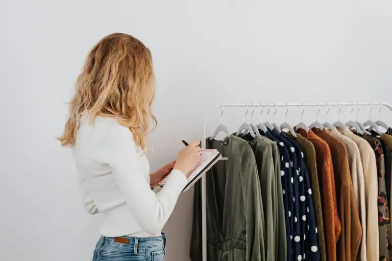 A woman takes notes while checking a rack of clothing