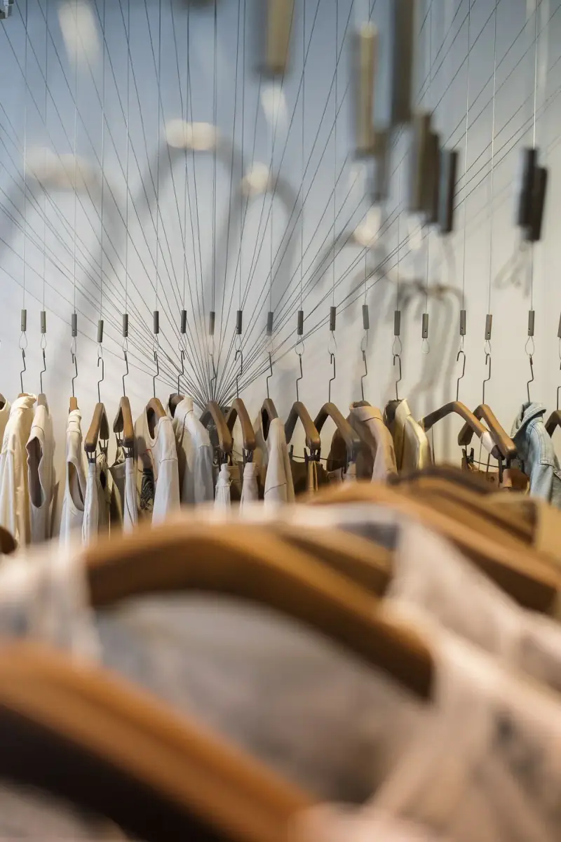 Neutral garments on wooden hangers hanging from a sculptural rail in a store
