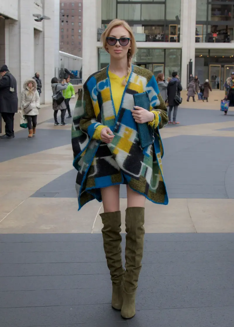 Woman in a plaid poncho, sunglasses and olive over-the-knee boots on a New York plaza