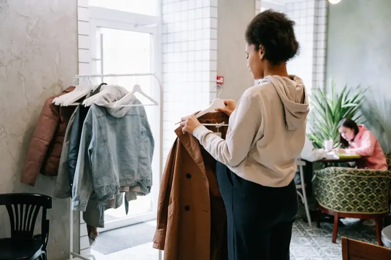 Woman holding up a brown coat while browsing a rack in a bright shop