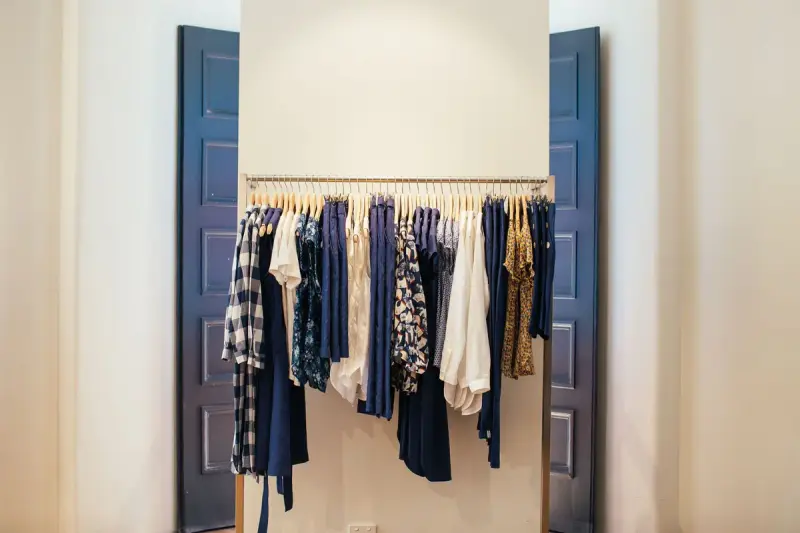 A single rail of mixed tops and dresses framed by tall blue doors in a white room