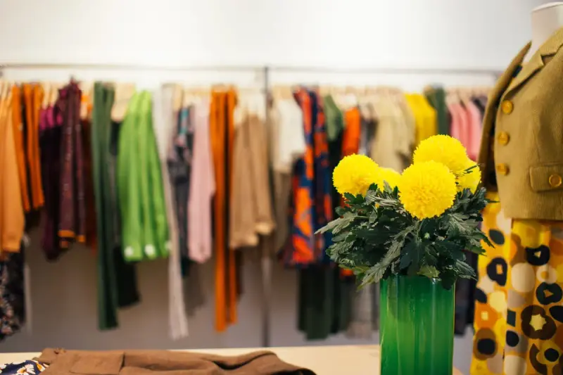 Brightly colored garments on a rail beside a vase of yellow flowers in a boutique
