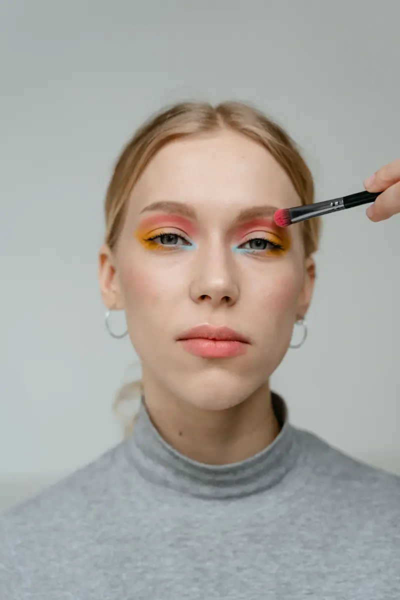 Woman with peach and yellow eyeshadow as a brush adds color to her lid