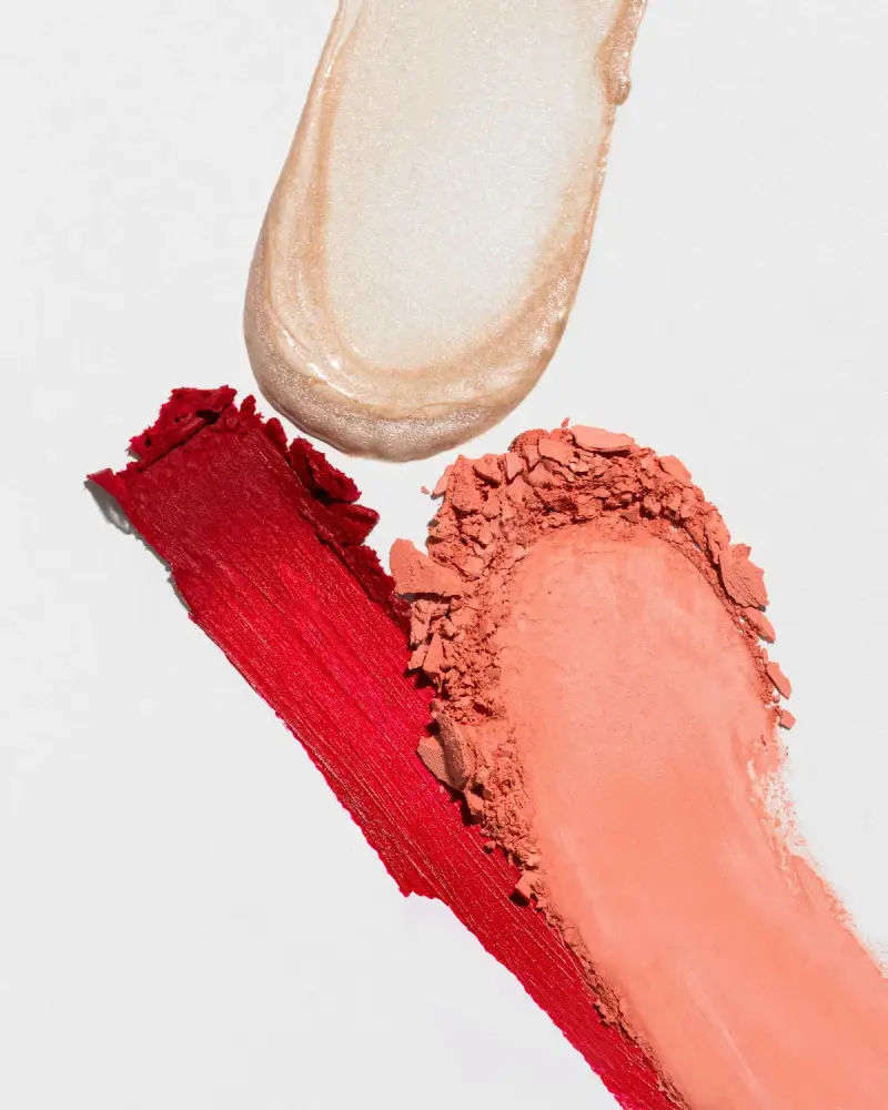 Swatches of highlighter, red lipstick and coral blush textures on white