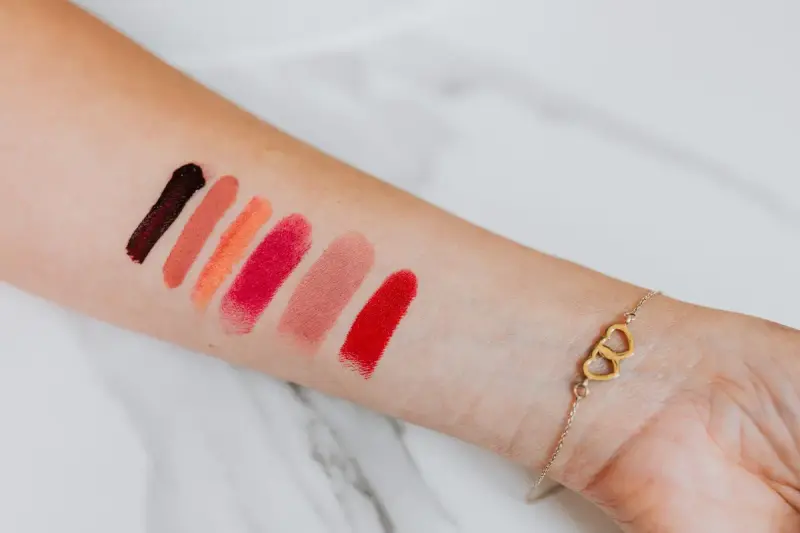 Lipstick swatches in red, coral and berry shades on a forearm