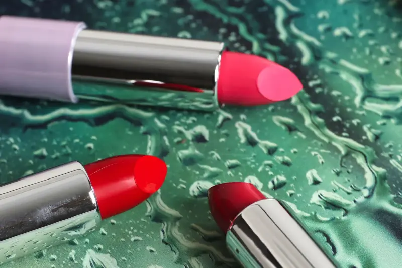 Three lipsticks in pink and red with metal cases on a wet green textured surface