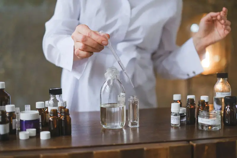 Formulator in a white coat transferring liquid with a glass pipette into small bottles