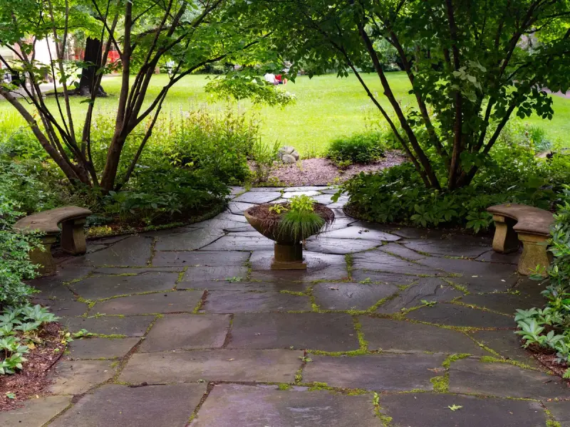 Flagstone patio with stone benches and a central planter surrounded by shade trees