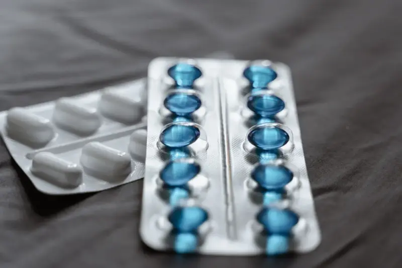 Blister packs of blue softgel capsules and white tablets on a dark fabric