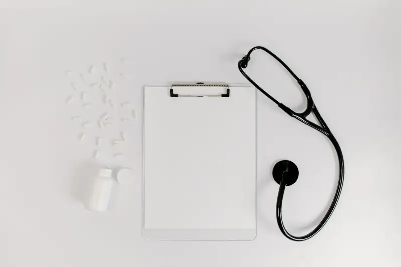 Clipboard with blank paper beside a stethoscope and pills on a flat surface
