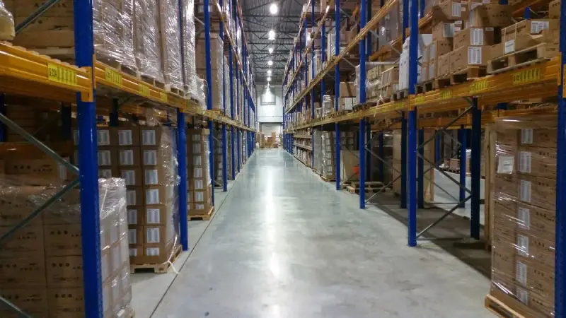 Long distribution center aisle lined with blue and yellow racks of shrink-wrapped cartons