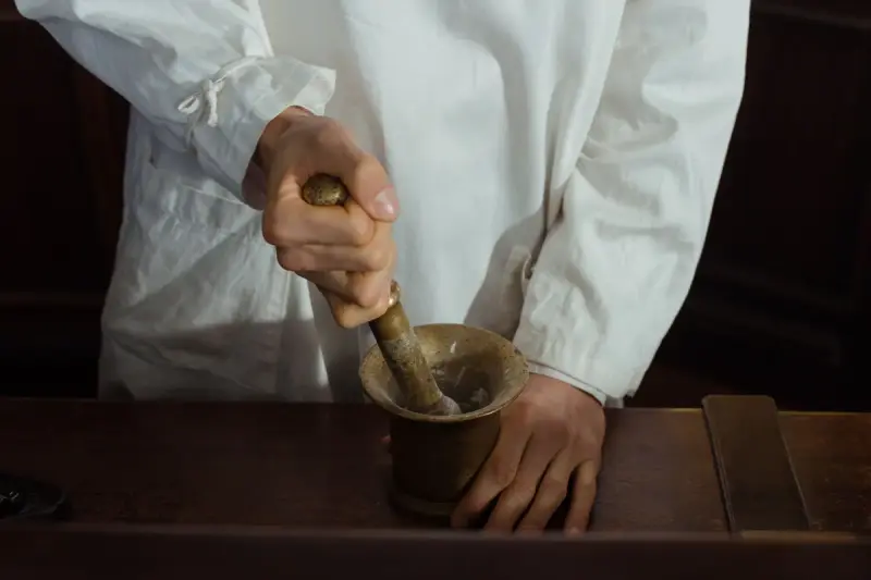 Hands grinding powder in a brass mortar and pestle on a dark wooden counter