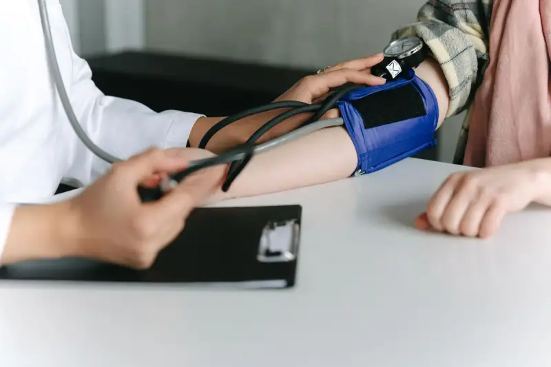 Clinician fitting a blue blood pressure cuff on a patient arm at a white table