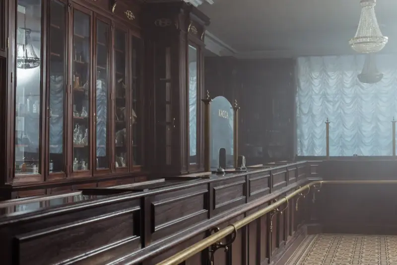 Long wooden pharmacy counter with glass-front cabinets and a chandelier in a classic drugstore interior