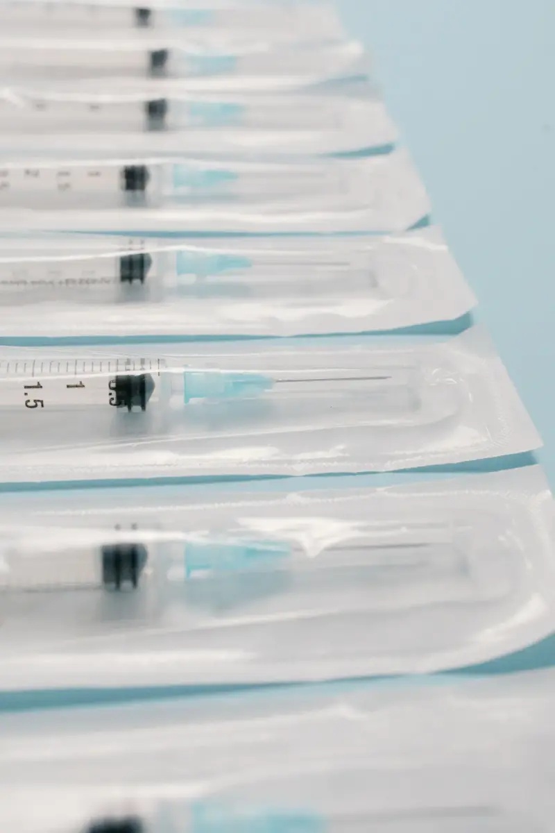Row of sterile syringes sealed in clear thermoformed blister packs on a pale blue surface