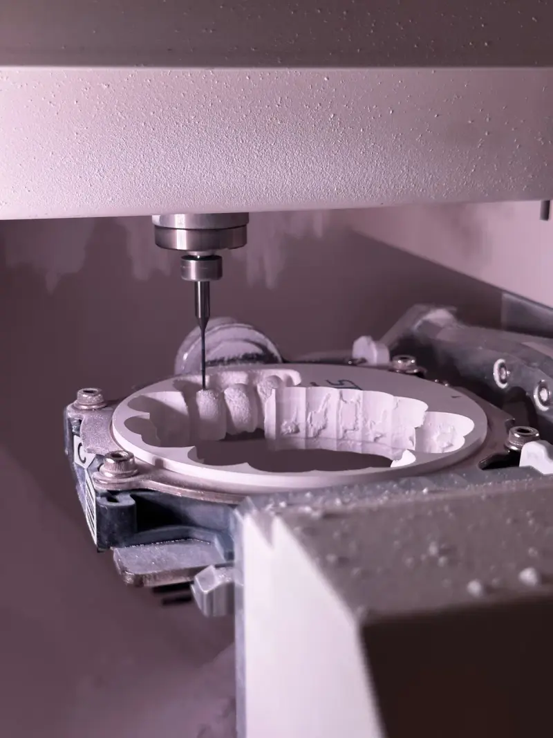 Fine CNC milling tool cutting dental shapes from a white ceramic disc in a fixture