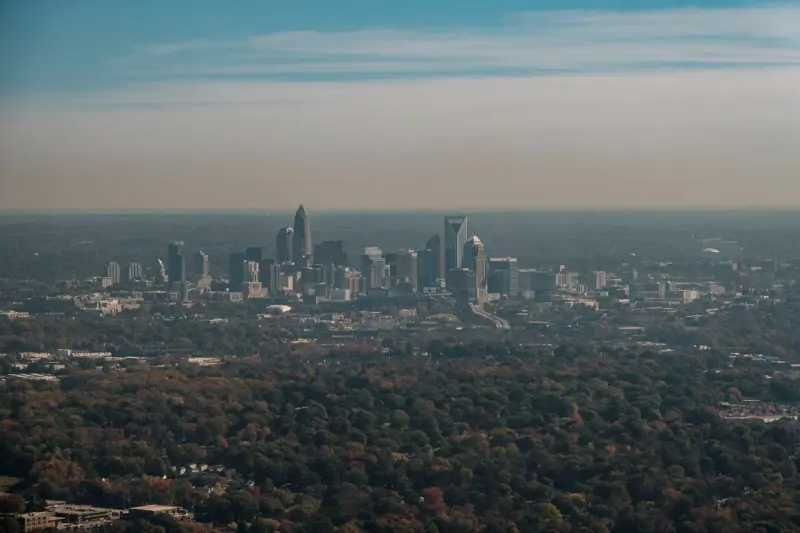 Aerial view of the Uptown Charlotte skyline rising above autumn tree canopy