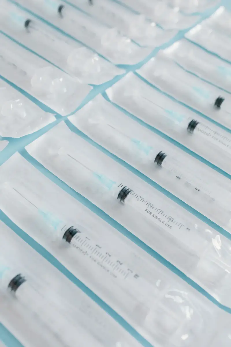 Rows of single-use syringes sealed in clear sterile pouches on a blue surface