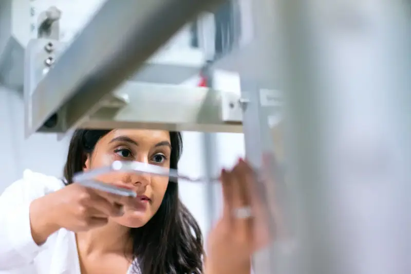 Engineer in a white lab coat adjusting a fine component on an aluminum test rig