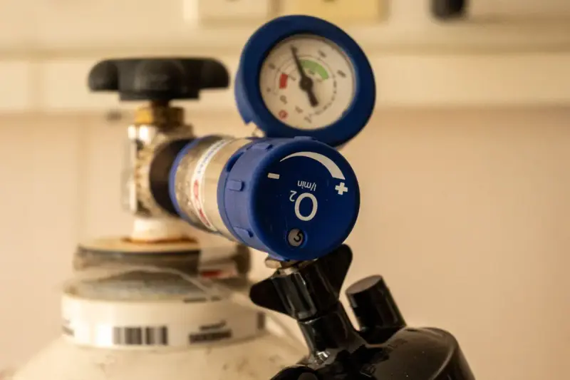 Blue oxygen flow regulator and pressure gauge fitted to the top of an oxygen cylinder
