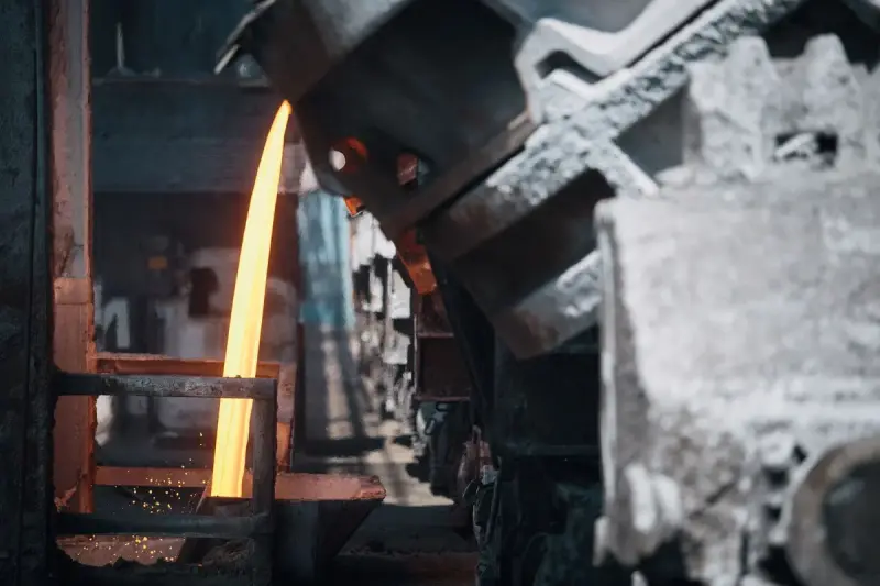 Molten metal pouring from a tilted vessel beside heavy ladles in a metal plant
