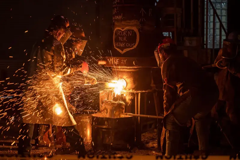 Foundry crew in protective gear pouring molten metal as sparks fly across the floor
