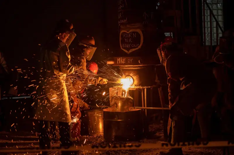 Foundry crew in protective coats and face shields pouring molten metal at night