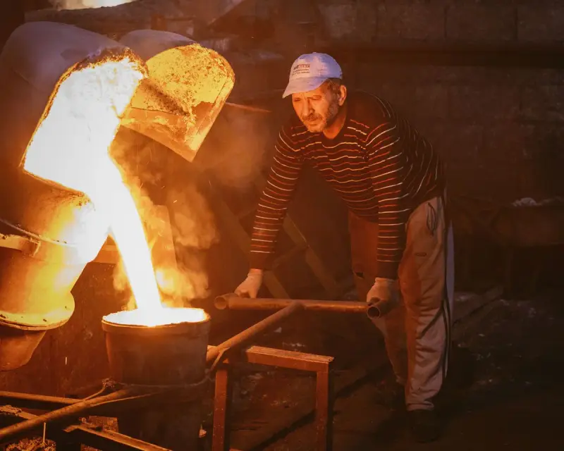 Metalworker guiding a ladle of molten metal into a mold in a foundry