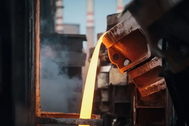 Bright stream of molten metal falling from a tilted ladle in a foundry