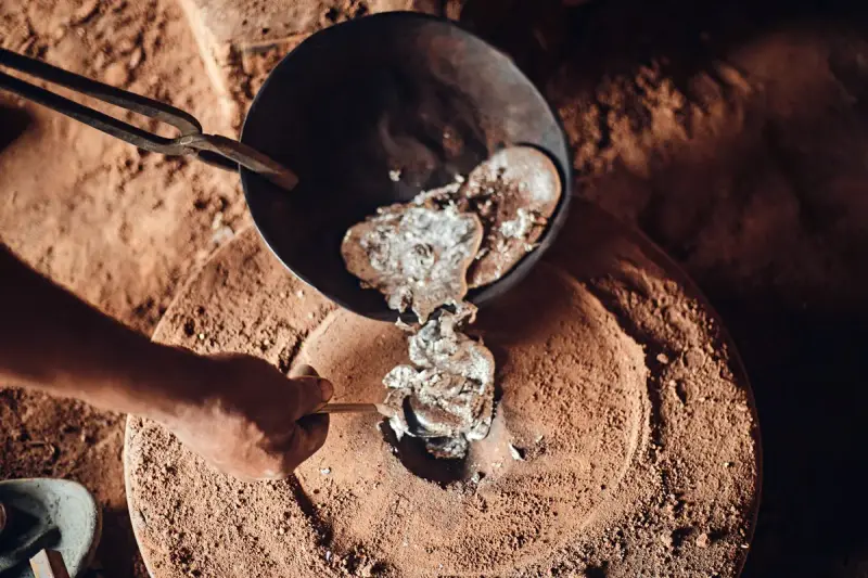 Molten aluminum poured from a small crucible into a round sand mold