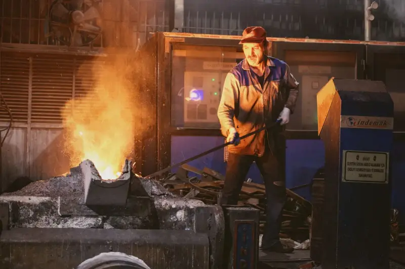 Foundry worker in a cap and work jacket tending a glowing furnace