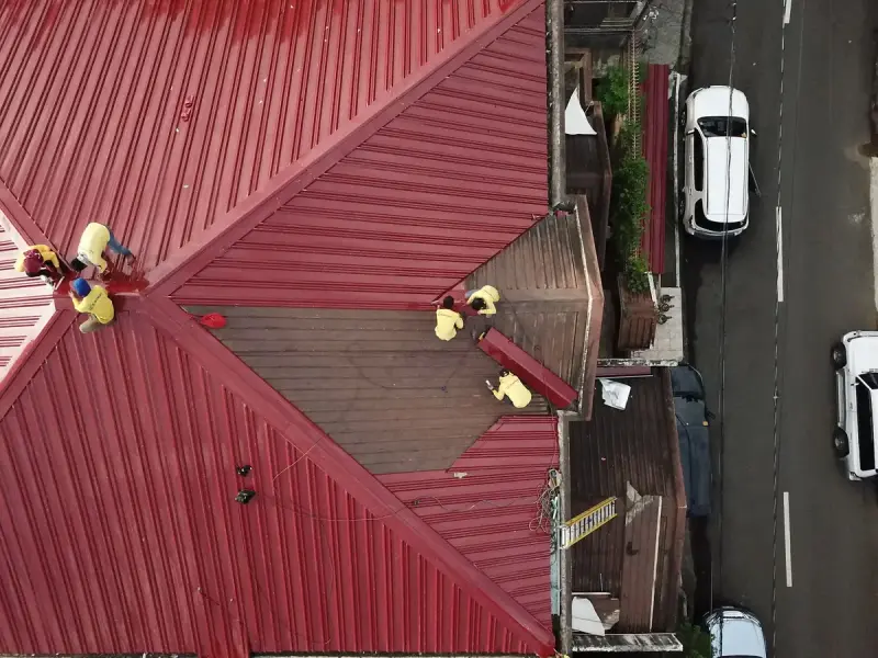 Aerial view of a crew working on a red standing-seam metal roof beside a city street