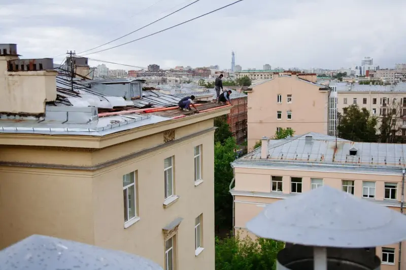 Workers repairing metal roofing on an old city building with metal rooftops all around