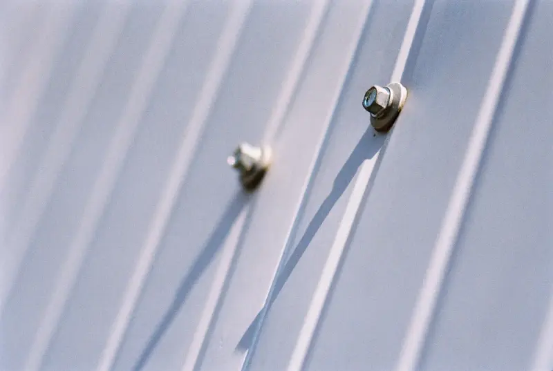Close-up of hex-head fasteners with washers holding a white ribbed metal panel