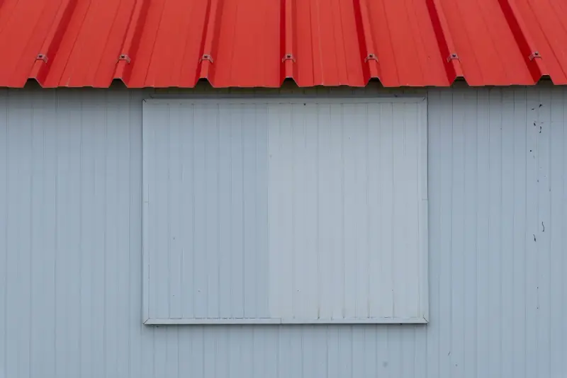 Red trapezoidal metal roof edge above a pale blue-grey vertical metal wall panel
