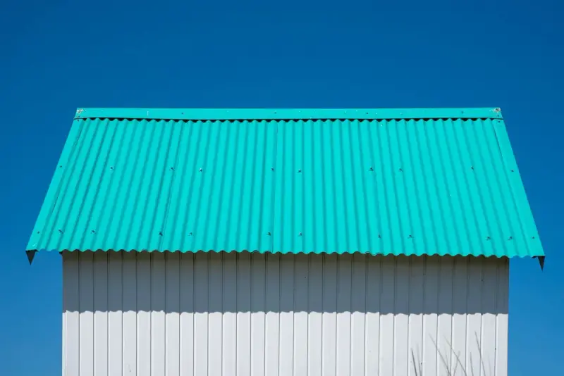 Teal corrugated metal gable roof over white vertical wall cladding against a blue sky