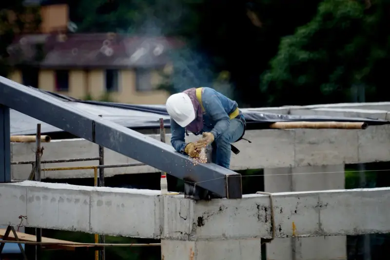 Worker in a white hard hat grinding a steel beam on a building frame