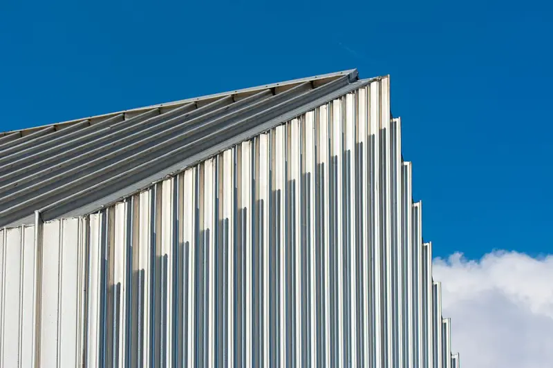 Silver corrugated metal roof and wall panels meeting at a sharp gable under a deep blue sky