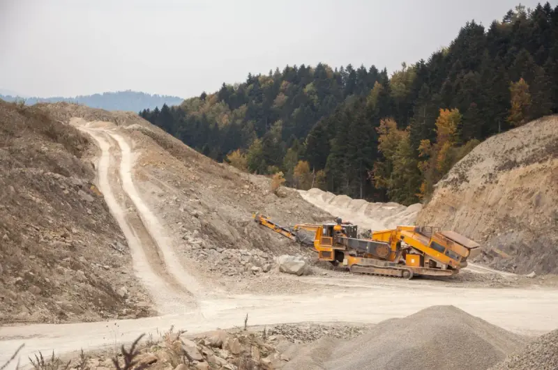 Tracked mobile crusher processing rock beside gravel piles in a quarry