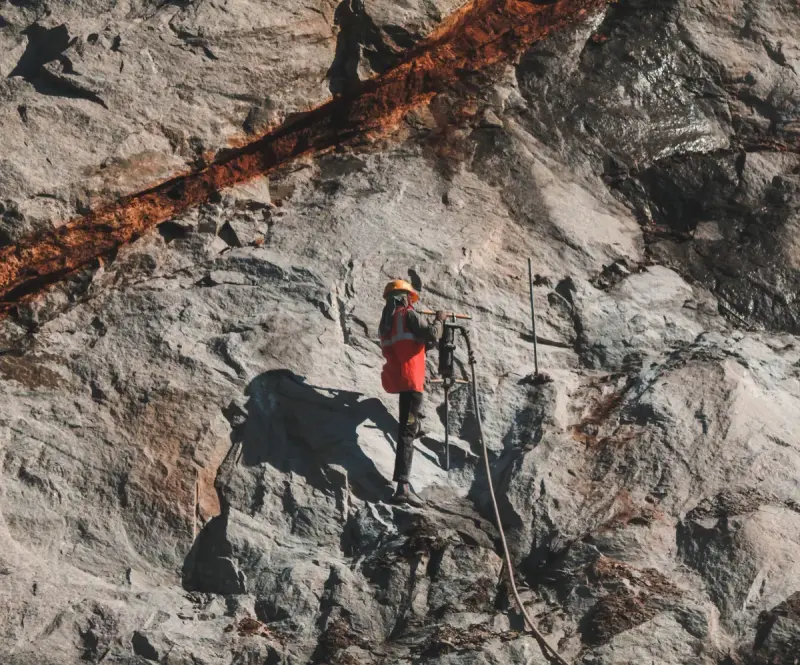 Driller in a hard hat and orange vest working on a steep rock face