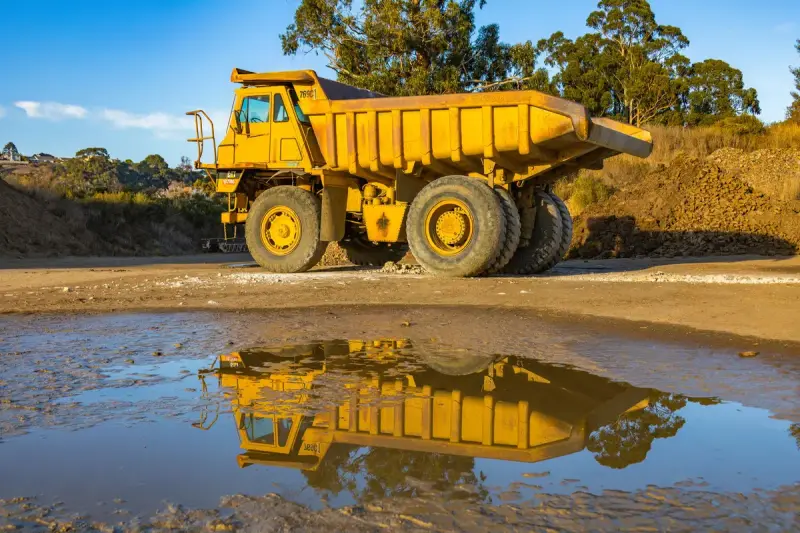 Yellow off-road dump truck reflected in a puddle at a mine site
