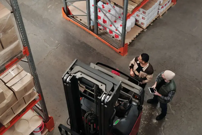 Overhead view of two warehouse workers with a tablet beside a reach truck