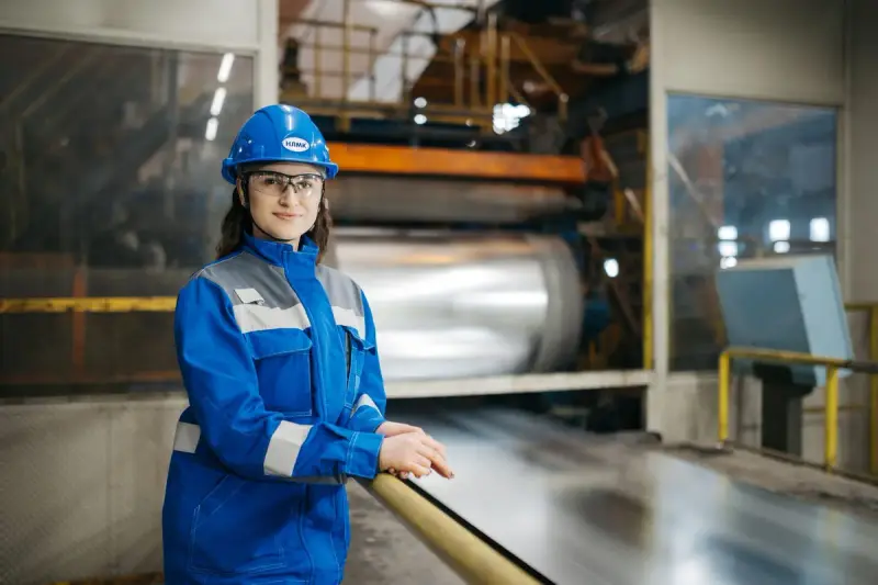 Female factory worker in blue uniform and safety gear inside an industrial plant