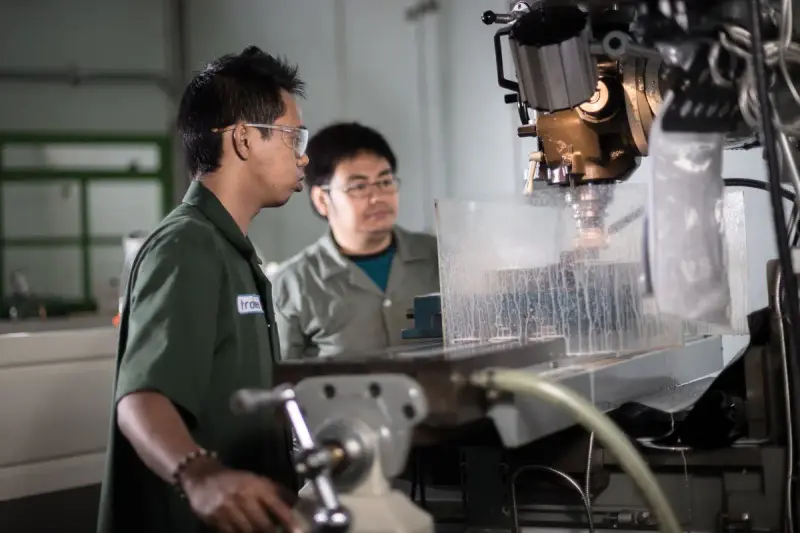 Two technicians in safety glasses watching a milling machine cut a part