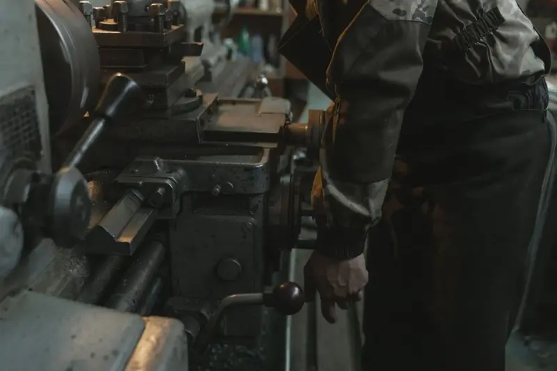 Machinist turning the handwheel of a manual lathe in a dim workshop