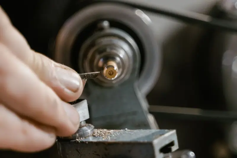 Fingers adjusting a small cutting tool against a spinning brass part on a lathe
