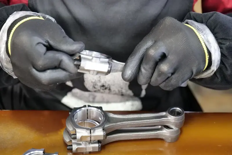 Gloved hands fitting a machined bearing cap onto a polished connecting rod