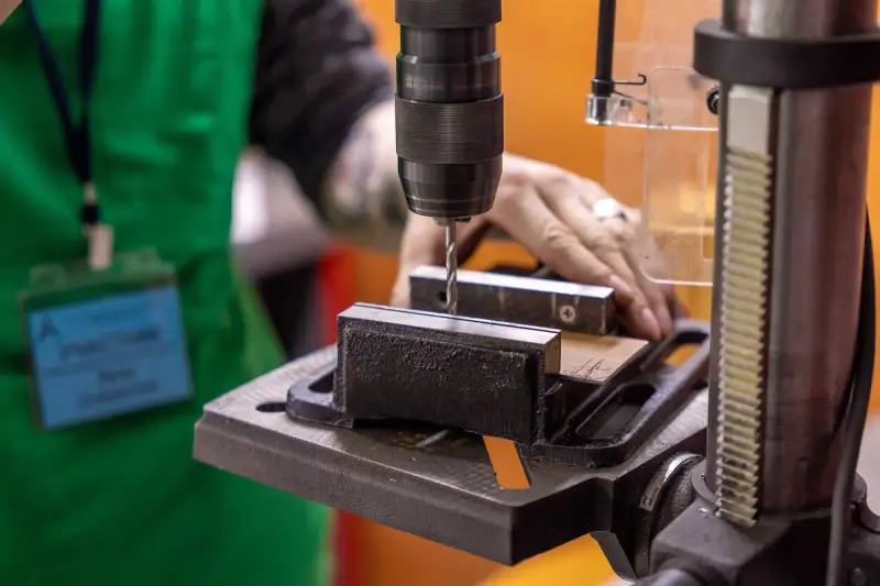 Drill press bit lowering into a steel block held in a machine vise