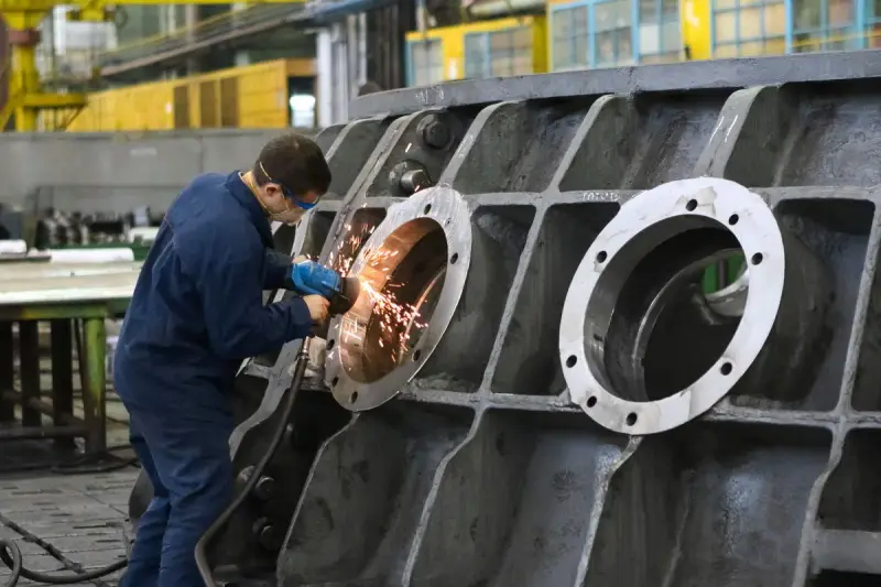 Worker in goggles and gloves grinding a bore on a large cast housing as sparks fly